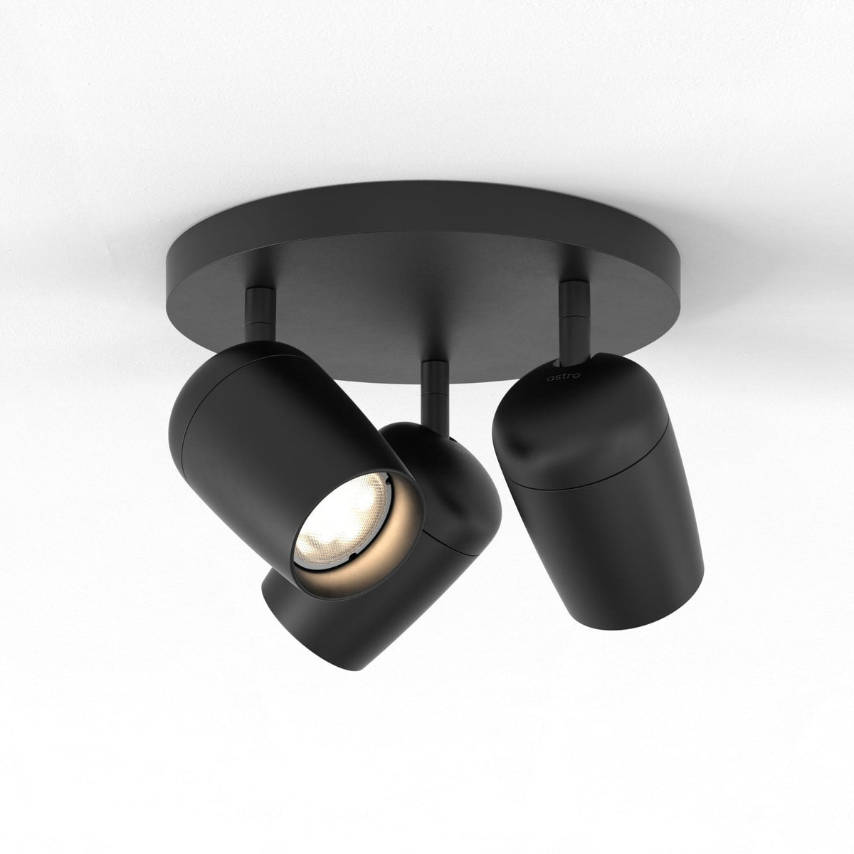 Three black cylindrical ceiling spotlights, one illuminated, on a white ceiling