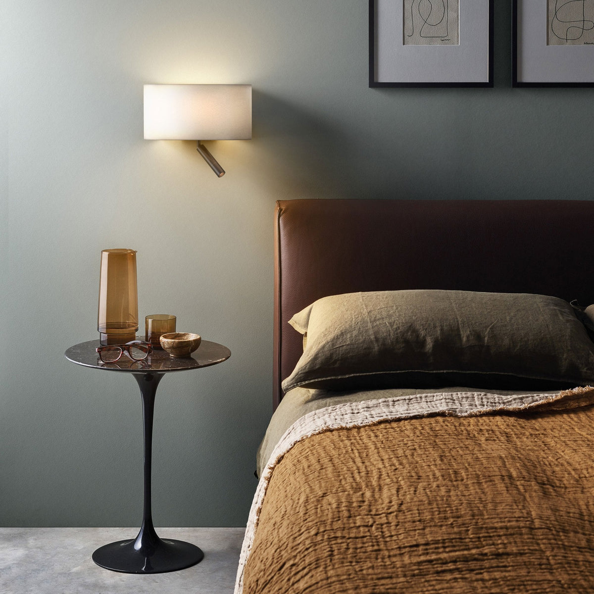 Bedroom with brown leather headboard, green wall, and black tulip side table with amber glass and glasses