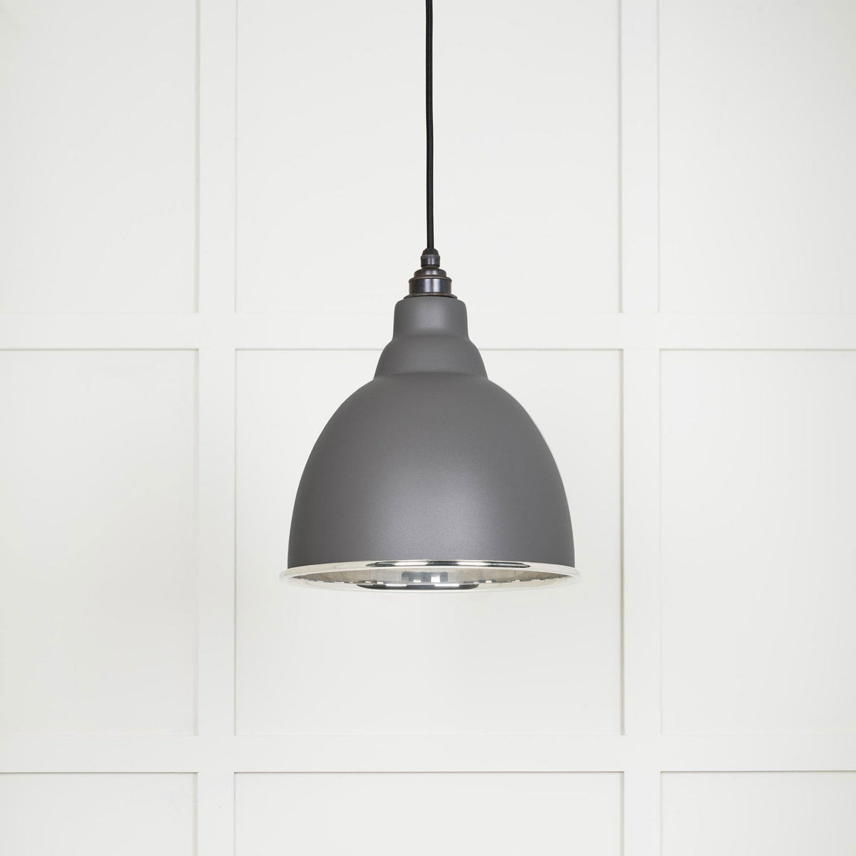 A dark grey dome-shaped pendant light with a silver interior, hanging against a white paneled wall.