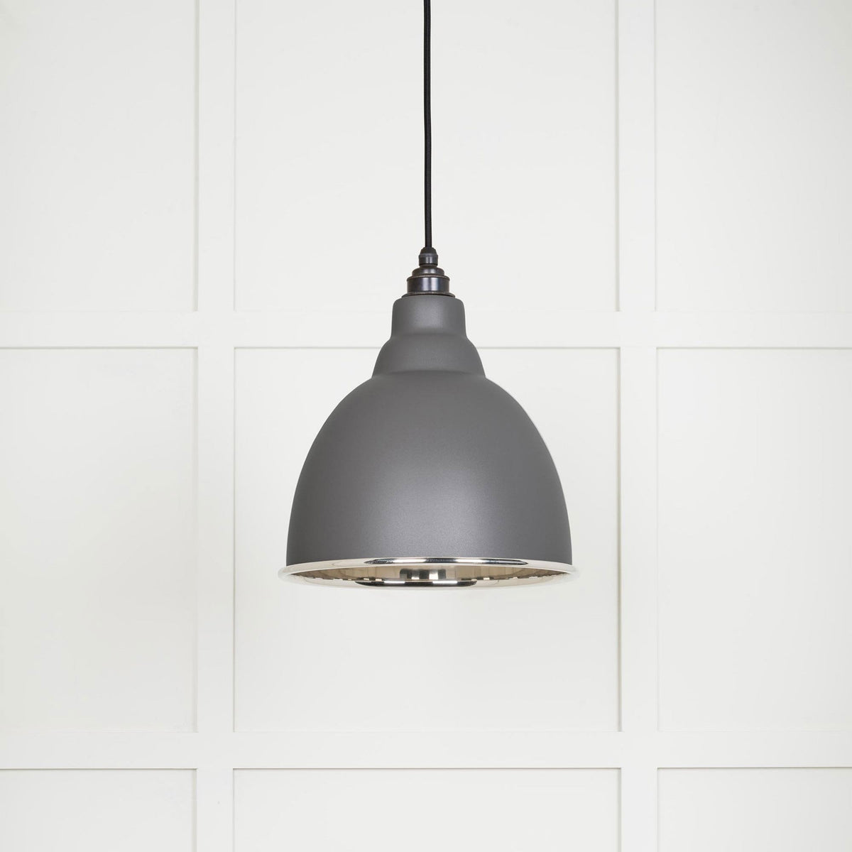 A dark grey dome-shaped pendant light with a silver interior, hanging against a white paneled wall.