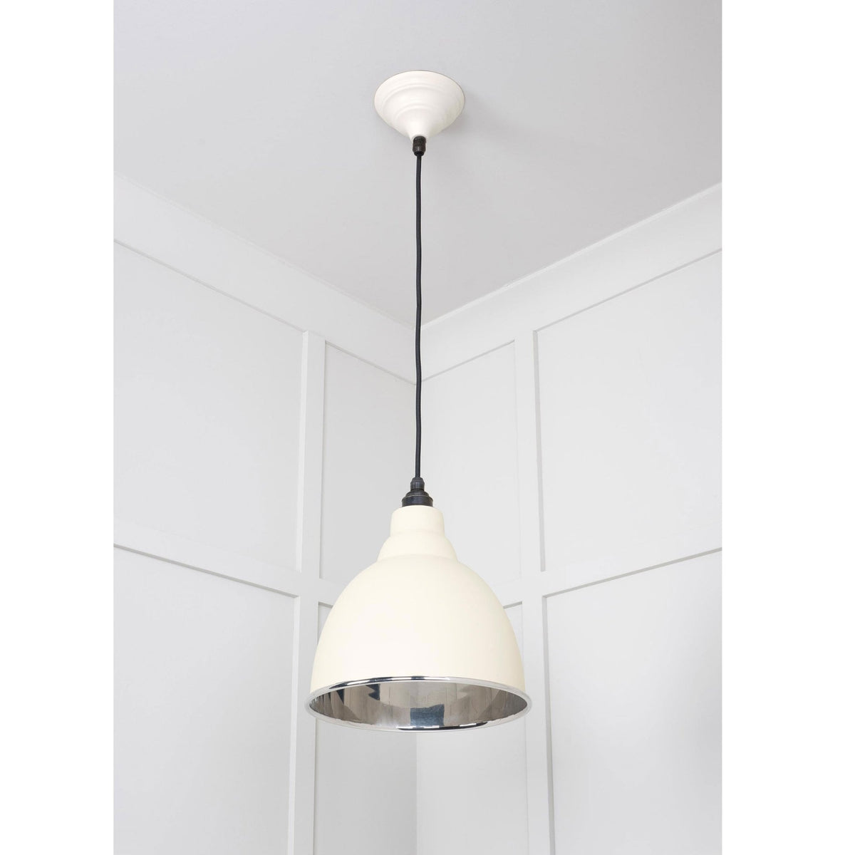 A cream pendant light with a white ceiling rose and black cable against a panelled wall.
