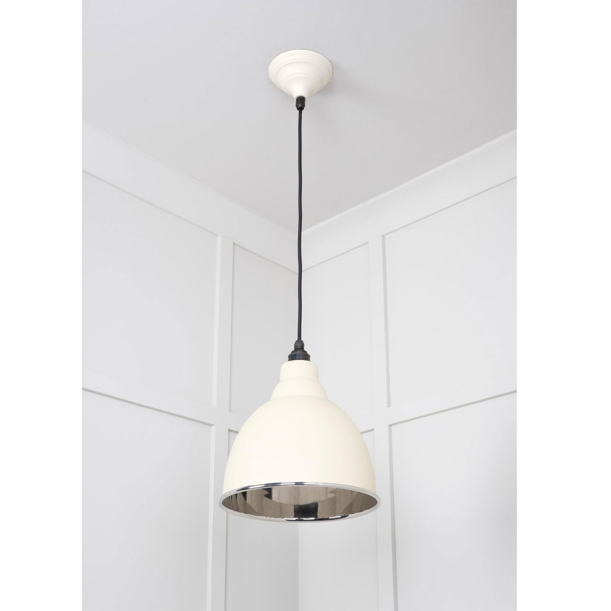 A cream pendant light with a white ceiling rose and black cable in a room corner.