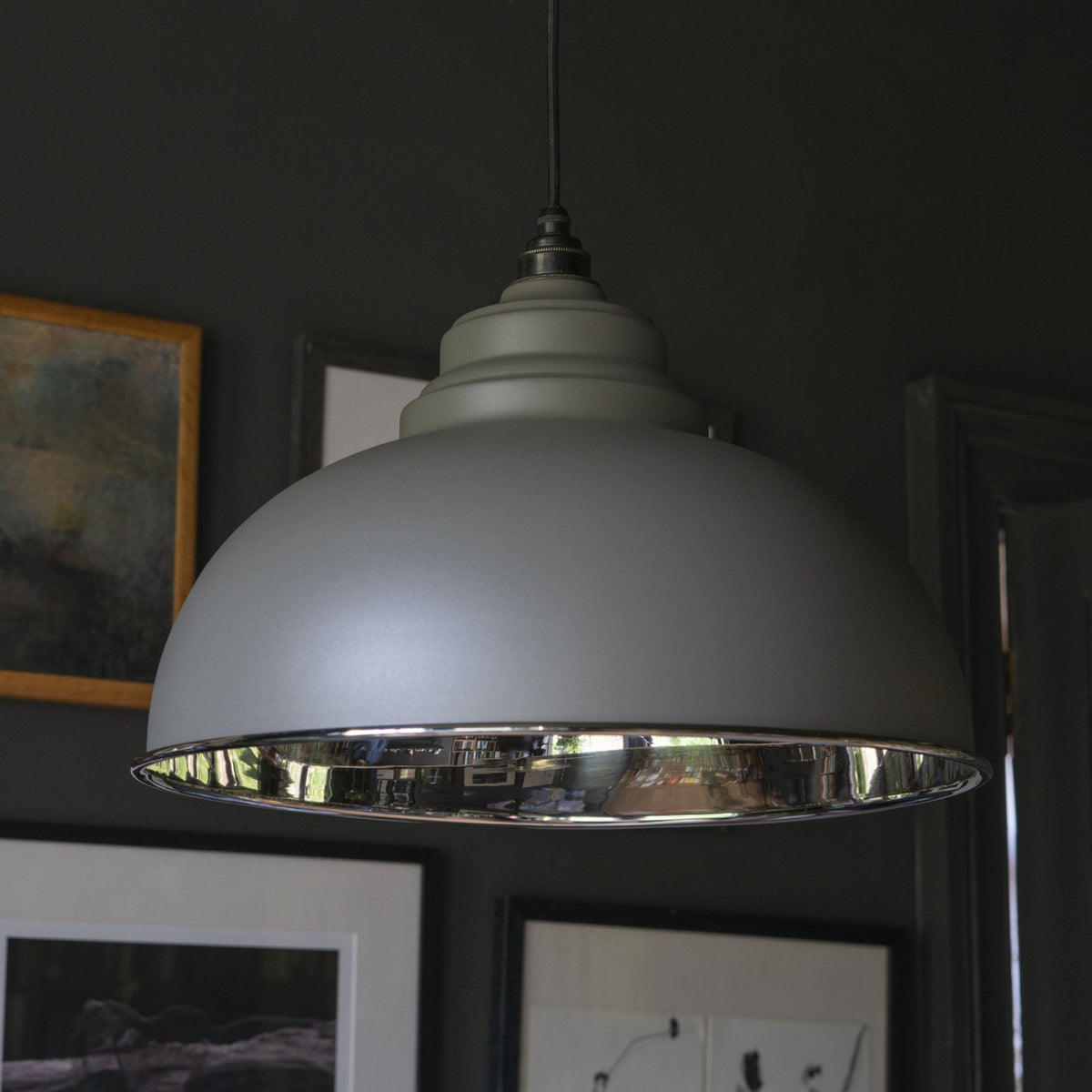 A large grey industrial-style pendant light with a reflective silver interior hangs in a dimly lit room.