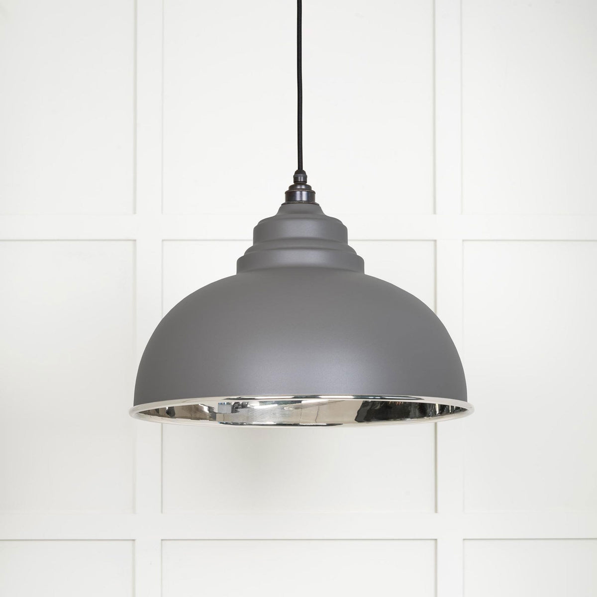 A grey industrial pendant light with a silver interior hangs against a white paneled wall.