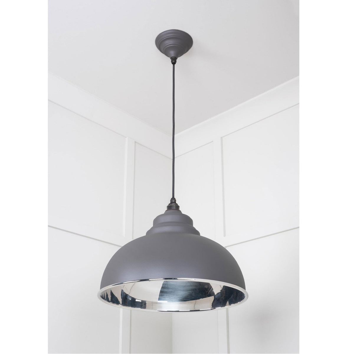 A full view of the grey industrial pendant light with a silver interior in a white room.