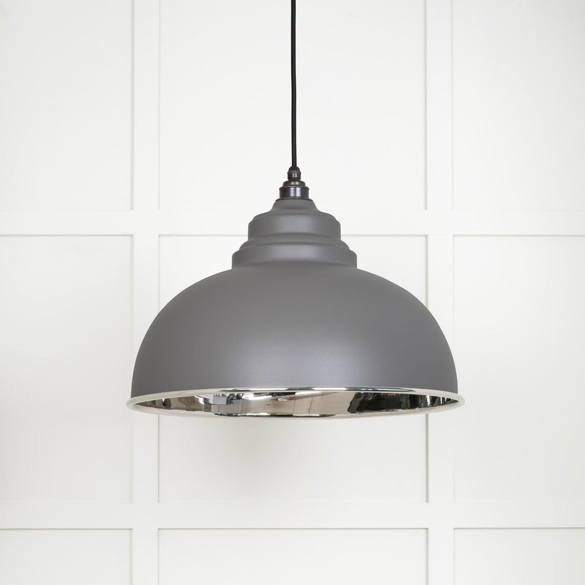 The grey industrial pendant light with a silver interior in a bright setting against a white wall.