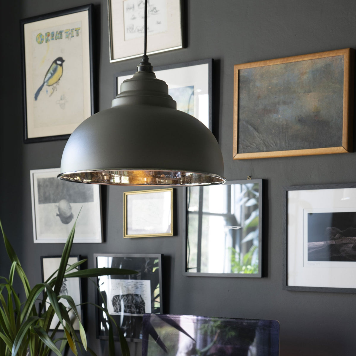 The grey industrial pendant light illuminating a dark room with a gallery wall of framed art.