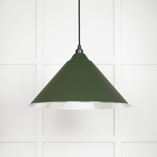 A dark green conical pendant light with a silver interior, hanging against a white paneled wall.