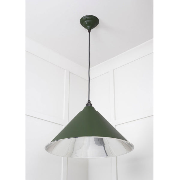 A dark green conical pendant light with a silver interior, hanging in a room corner.
