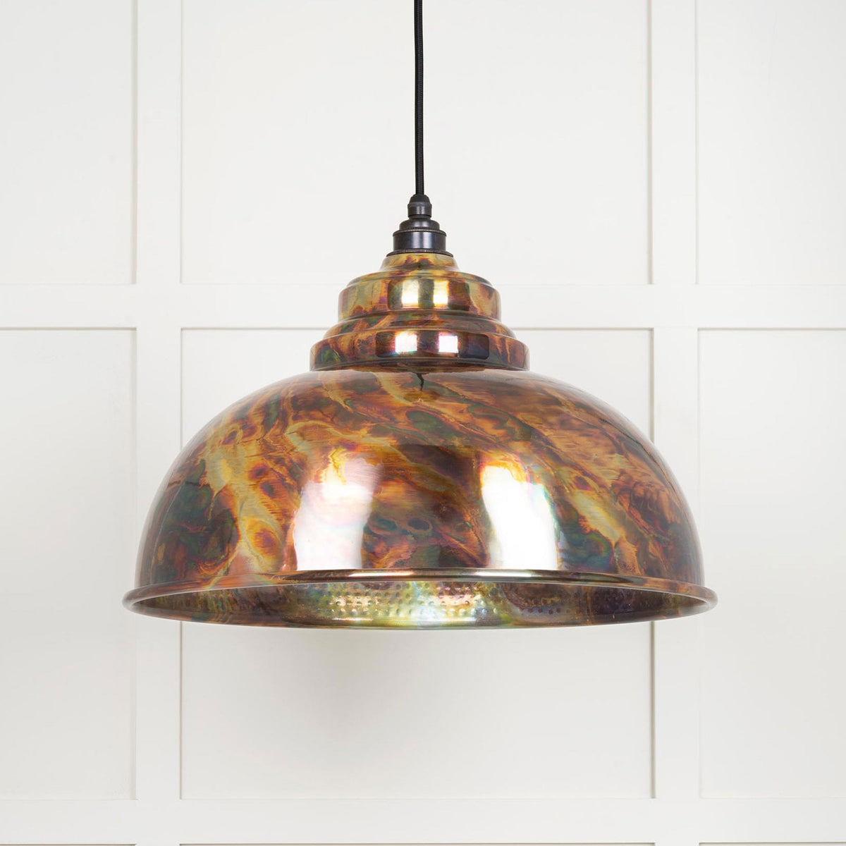 Dome pendant light with an iridescent, multicoloured, metallic shade hanging against a white wall.