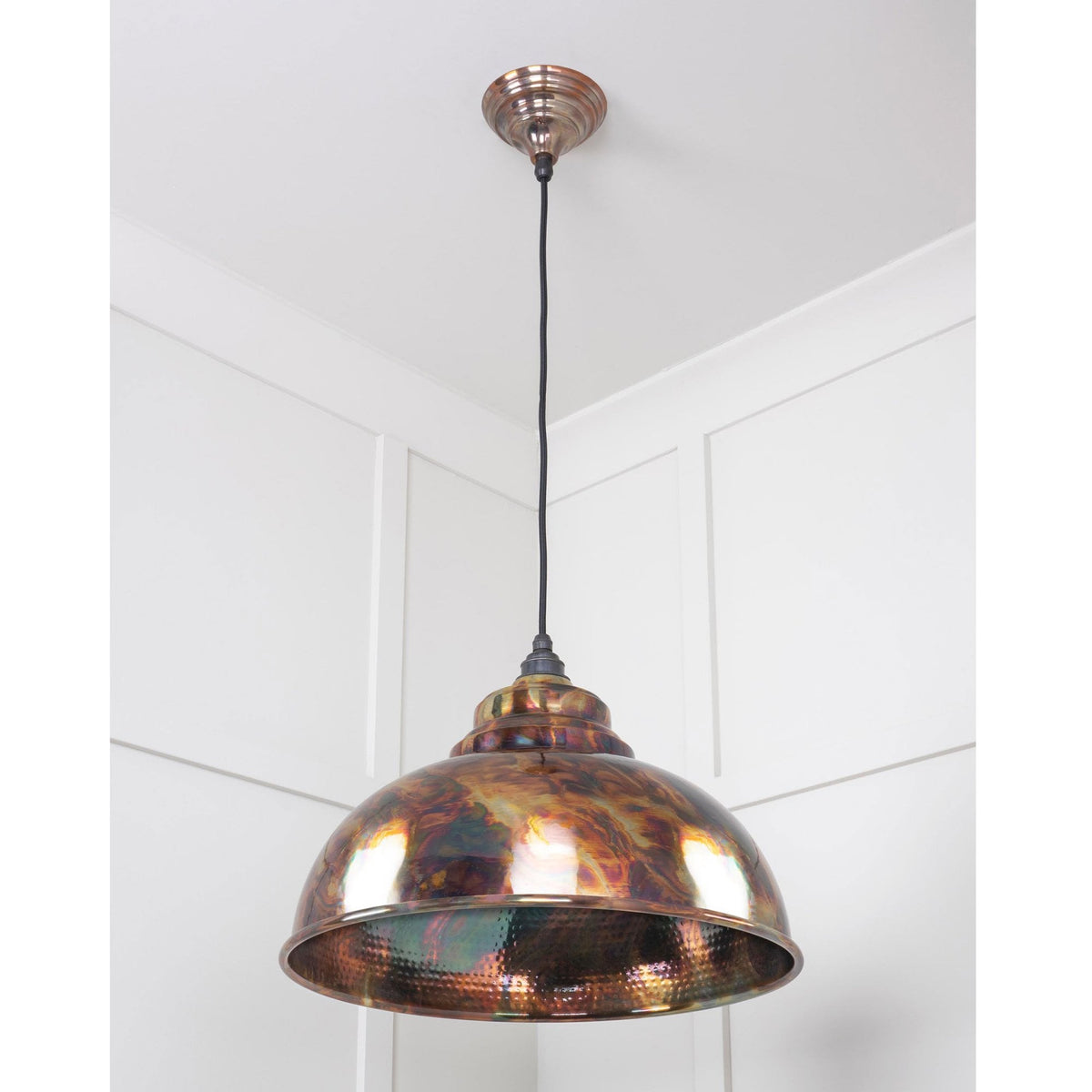 Dome pendant light with an iridescent, multicoloured, metallic shade against a white ceiling.