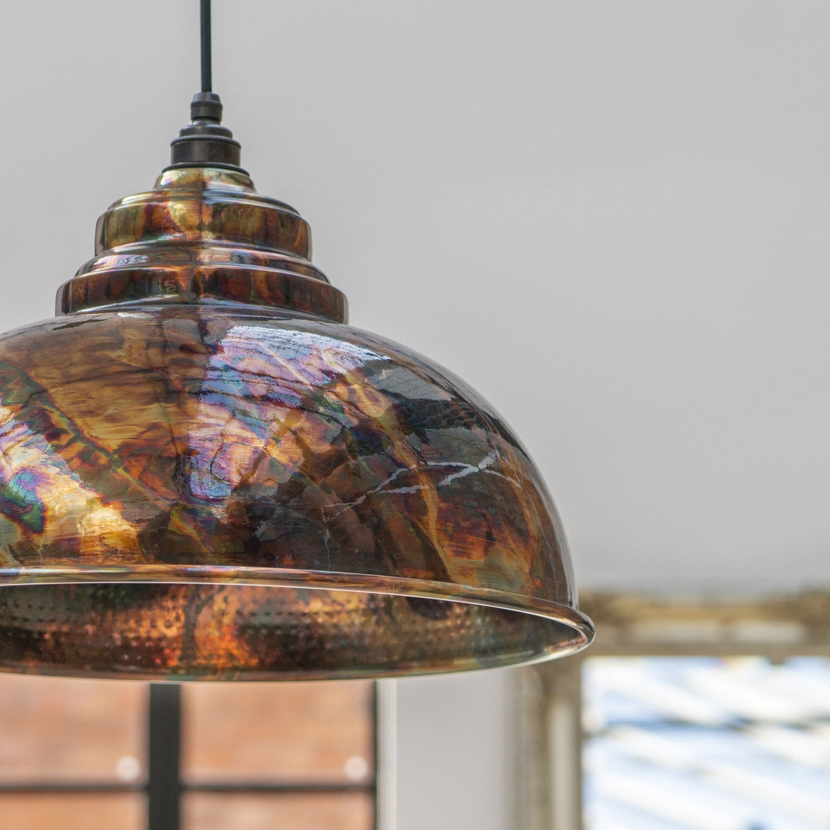 Dome pendant light with a metallic, iridescent, multicoloured finish in a room with a window.