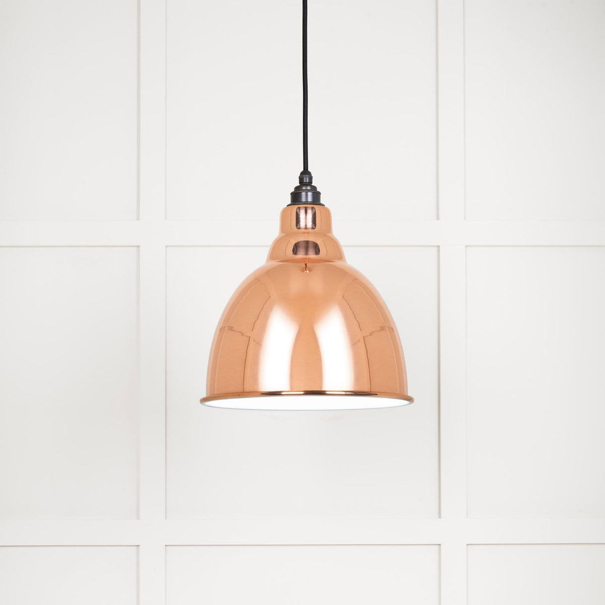 A close up of a shiny copper ceiling pendant light with a black cord.