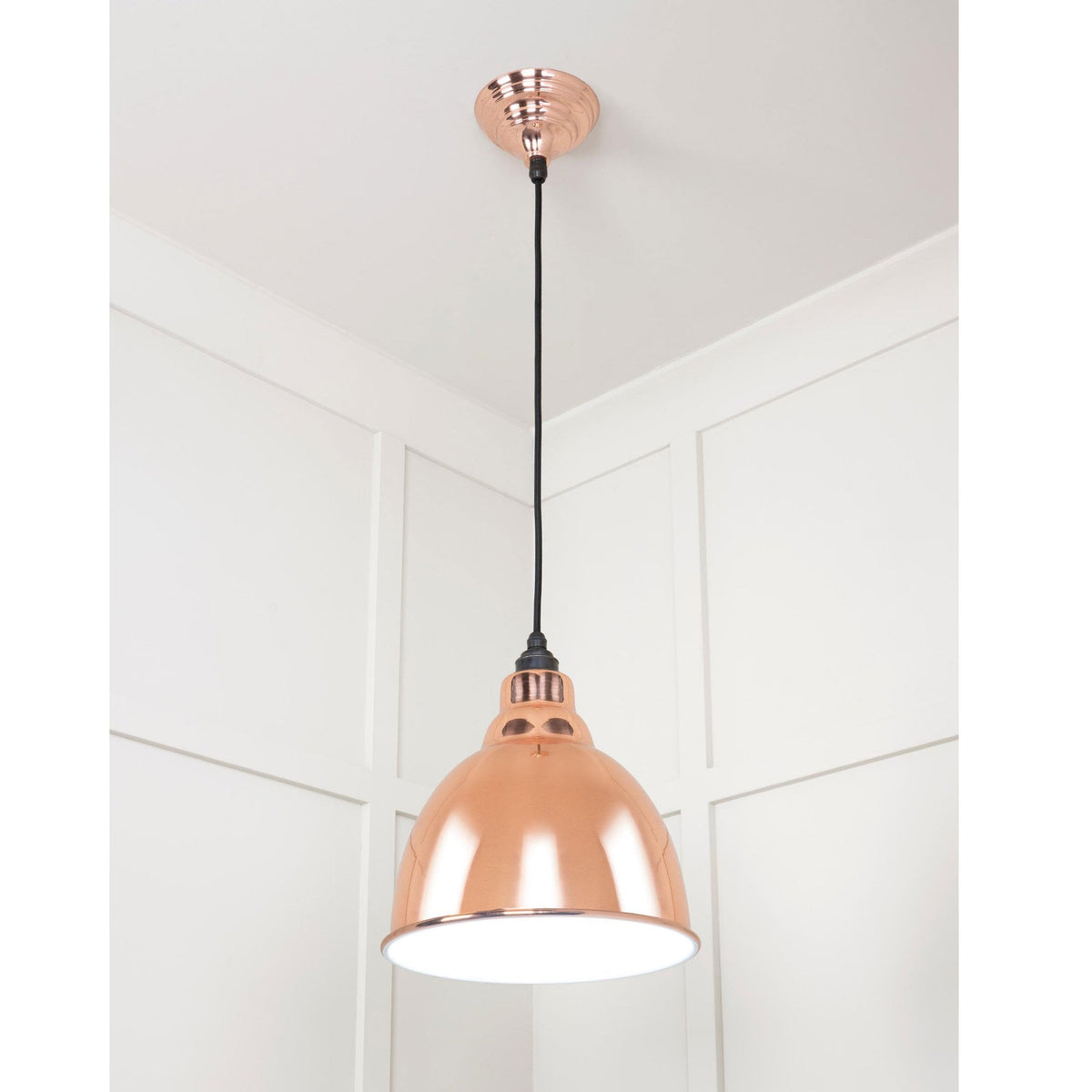 A shiny copper ceiling pendant light hanging in a room with white panelled walls.
