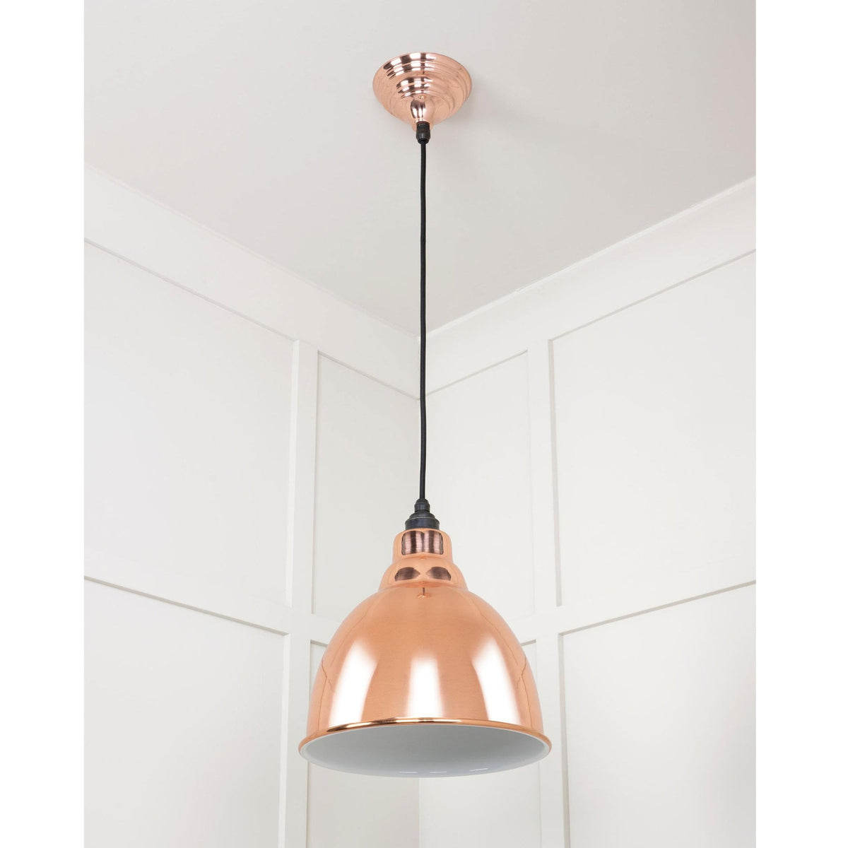A copper pendant light hanging from a ceiling with white panelled walls.