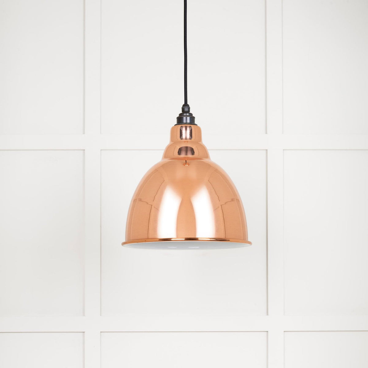 A single copper pendant light with a black flex against a white panelled wall.