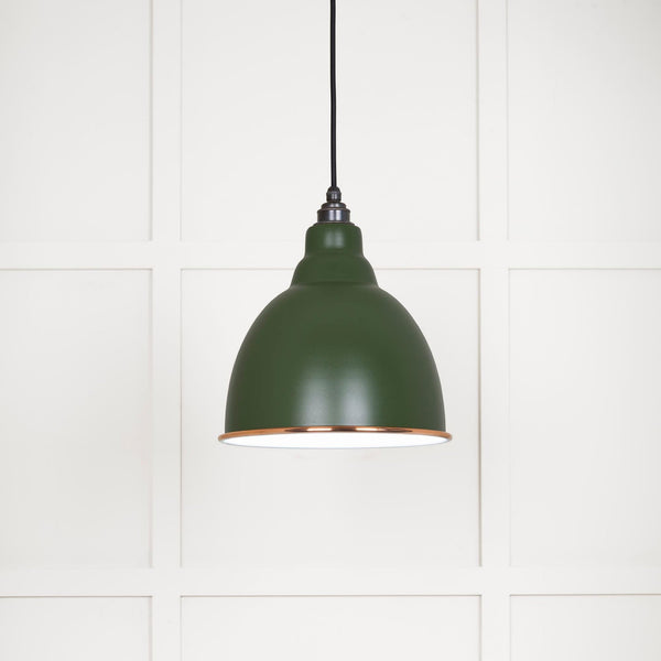 A close-up of a green industrial pendant light with a copper rim.