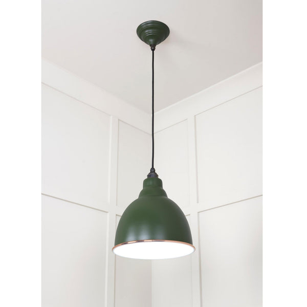A green industrial pendant light with a copper rim hangs from a white ceiling.