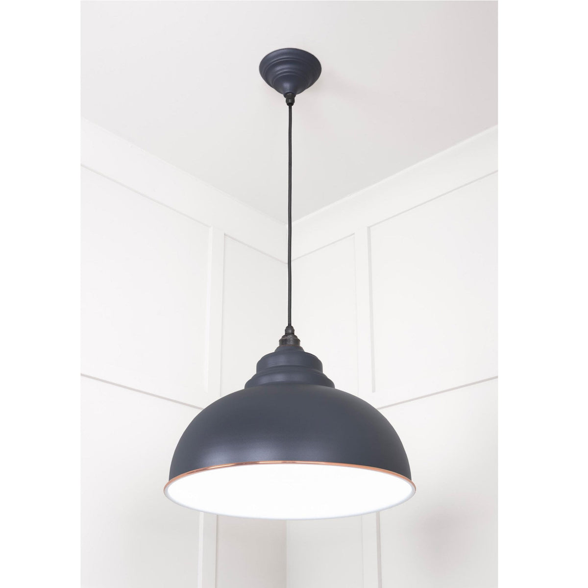 The Oxford pendant light hangs in a room with a white panelled wall.