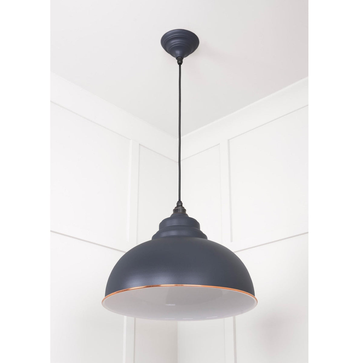 The Oxford pendant light hangs in a room with a white panelled wall.