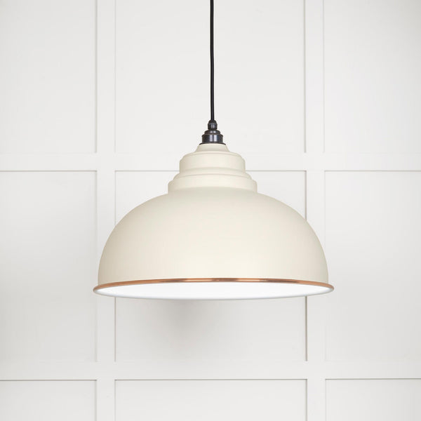 A close up of a white and copper pendant light against a white panelled wall.