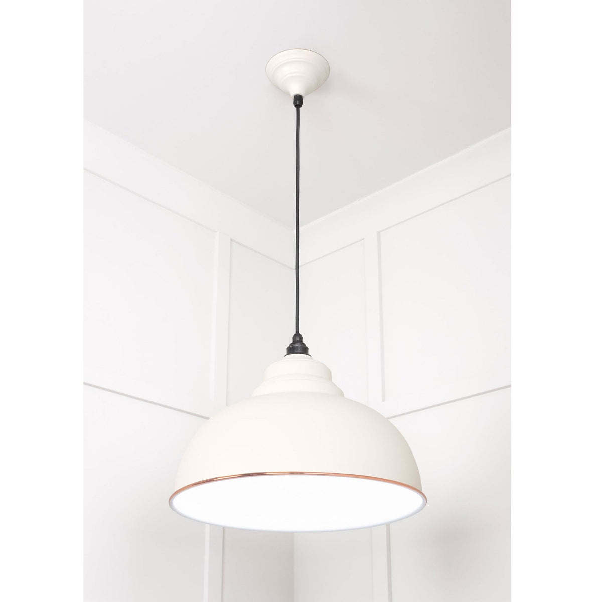 A white and copper pendant light hanging in a room with white panelled walls.