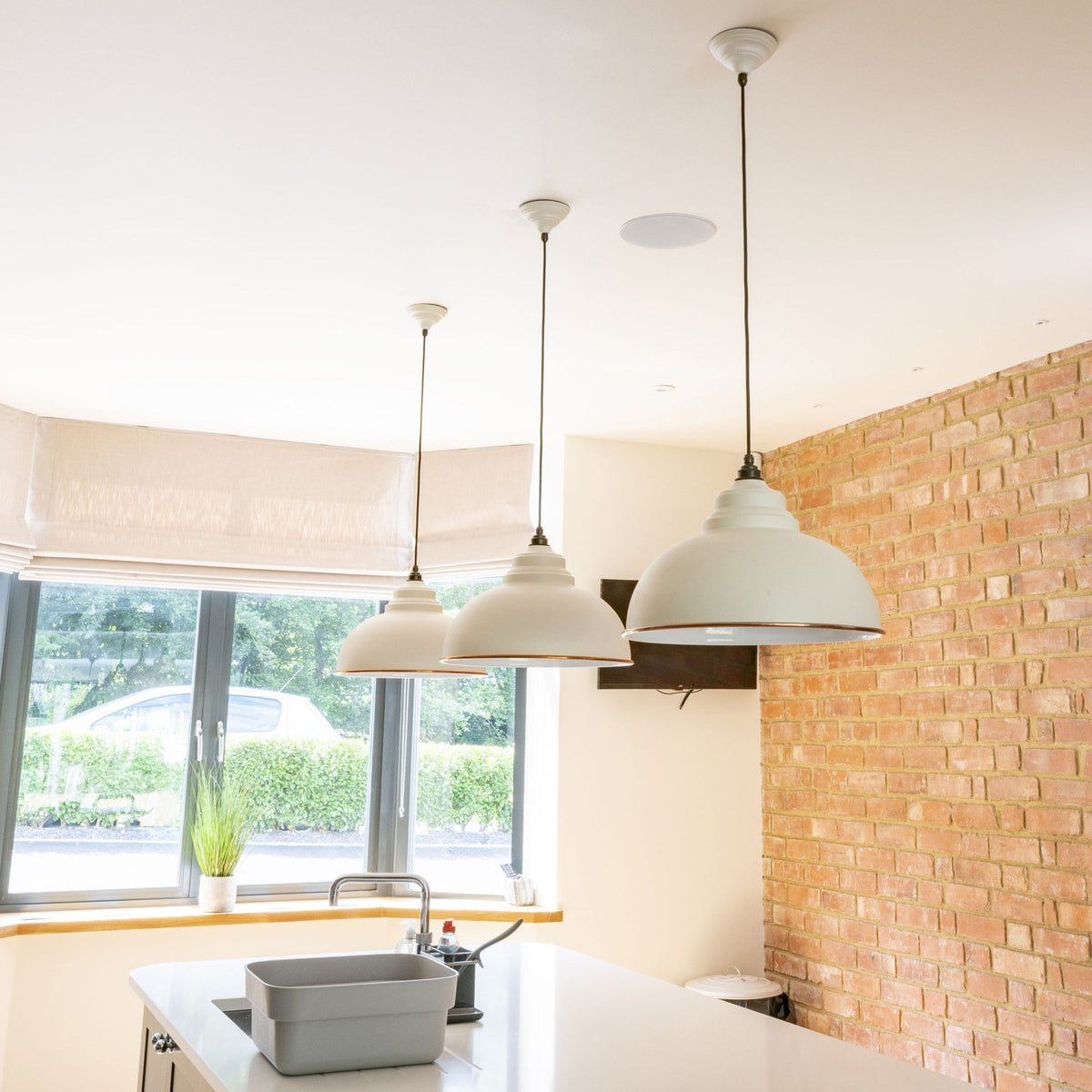 Three white and copper pendant lights hanging above a kitchen island with a brick wall.