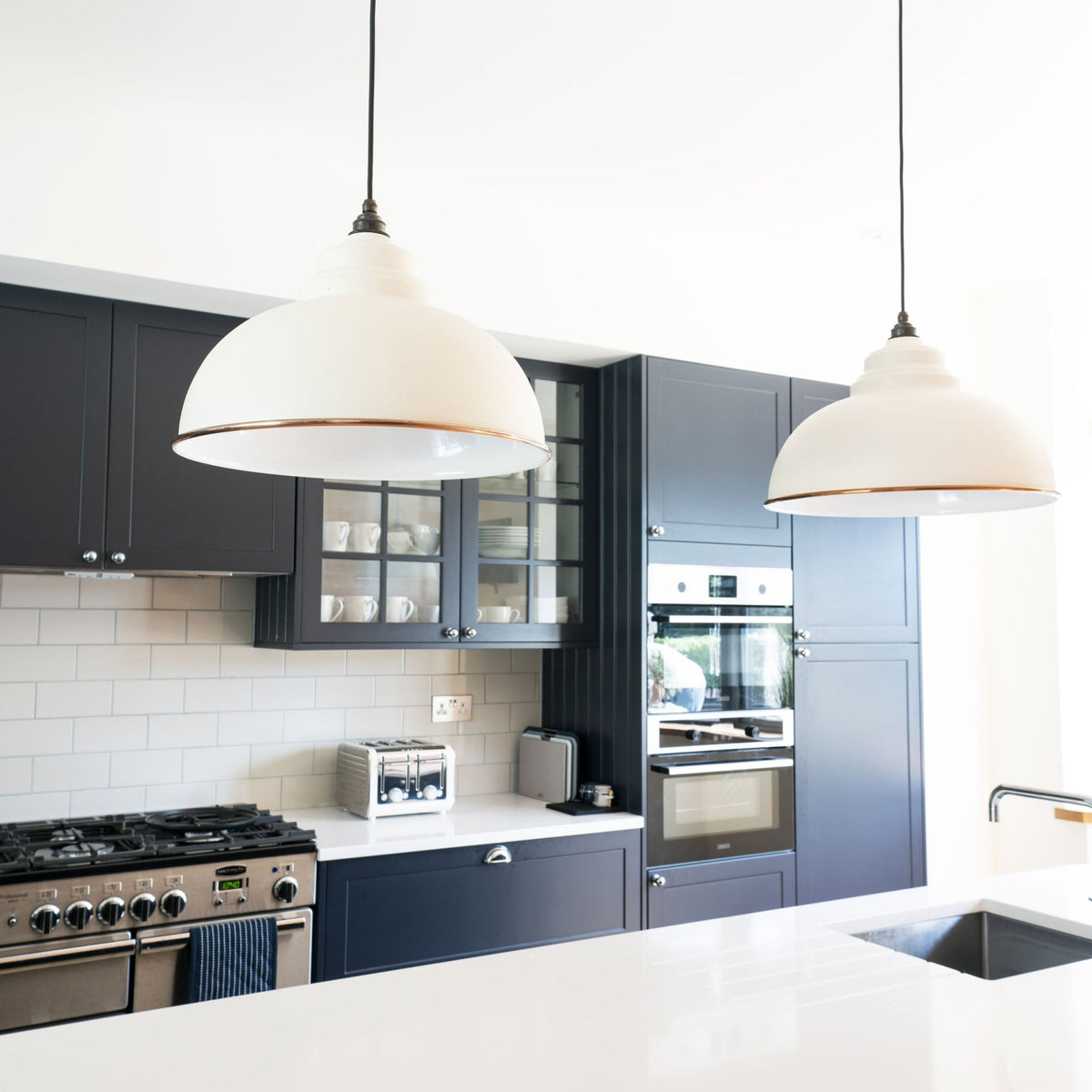 Two white and copper pendant lights hanging above a kitchen island with dark blue cupboards.