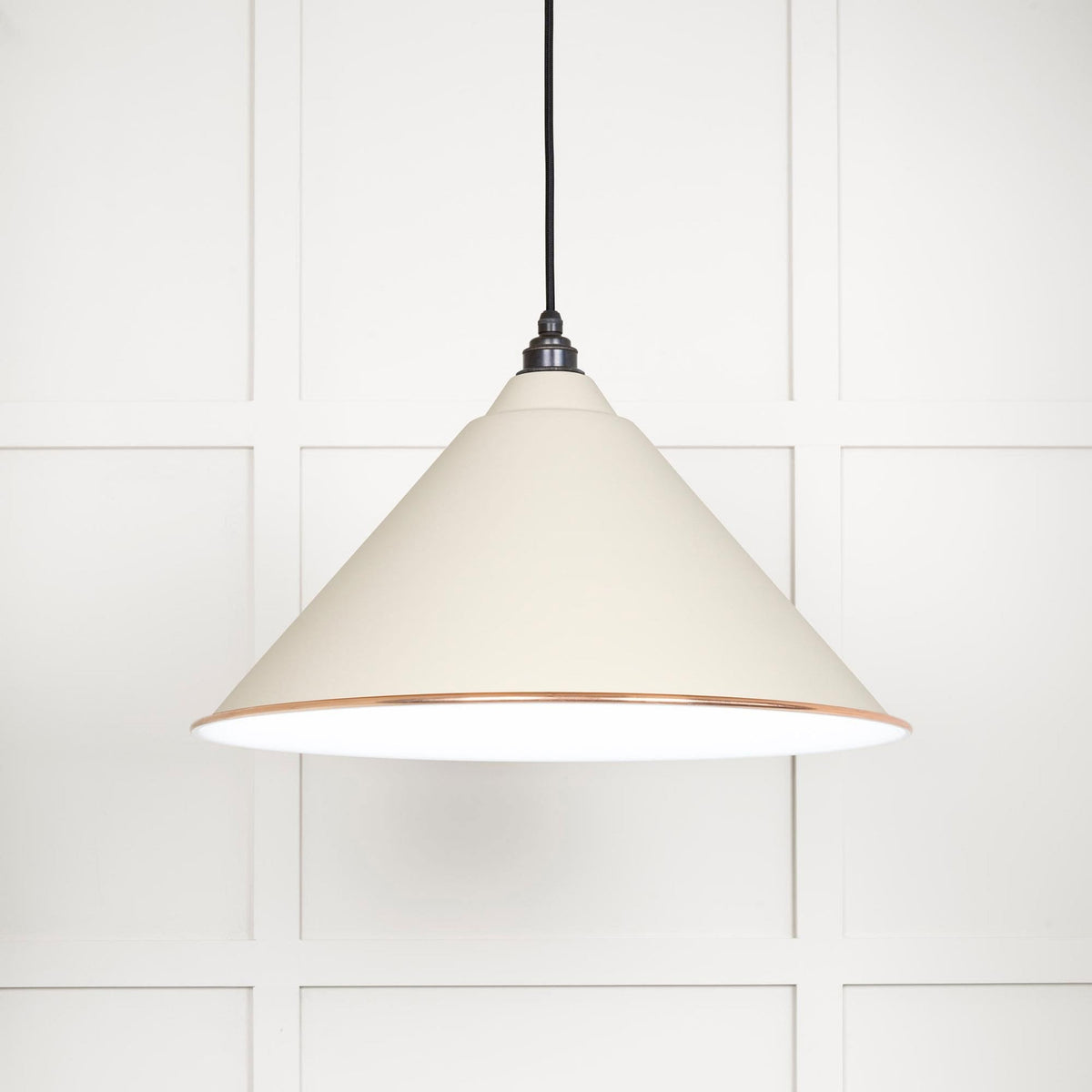 A white conical pendant light with a copper band hangs against a panelled white wall.