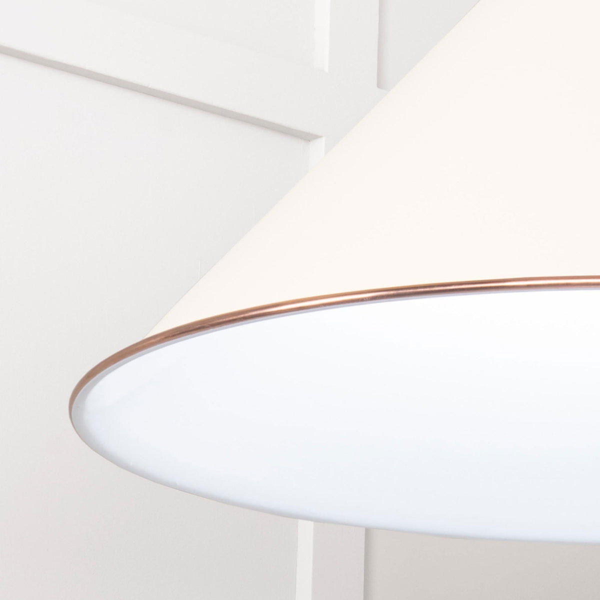 A close-up of the white conical pendant light, highlighting the copper band.