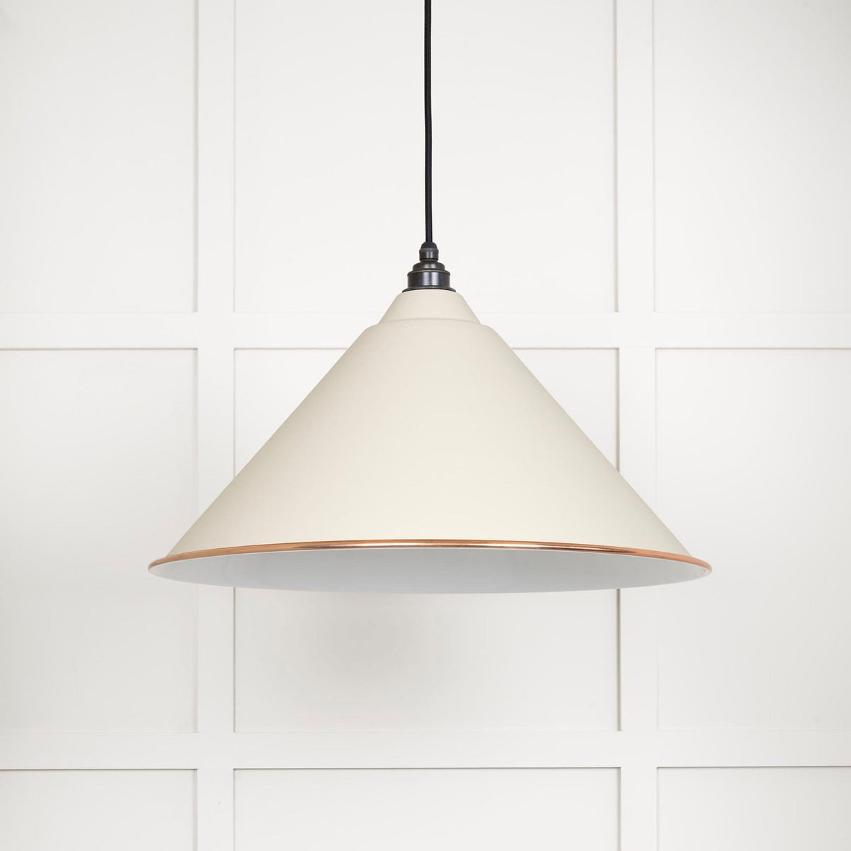 A white conical pendant light with a copper band hangs against a panelled white wall.
