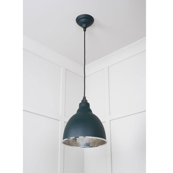 A dark green pendant light hangs elegantly in a room with white paneled walls. 
