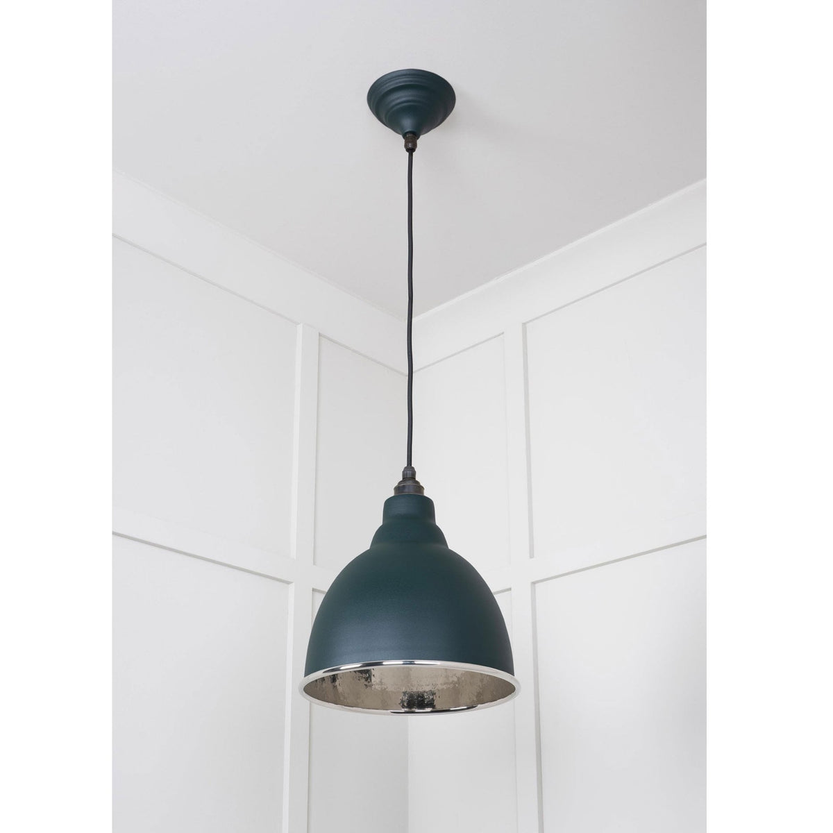 A dark green pendant light suspended against white paneled walls, with a contrasting silver interior. 