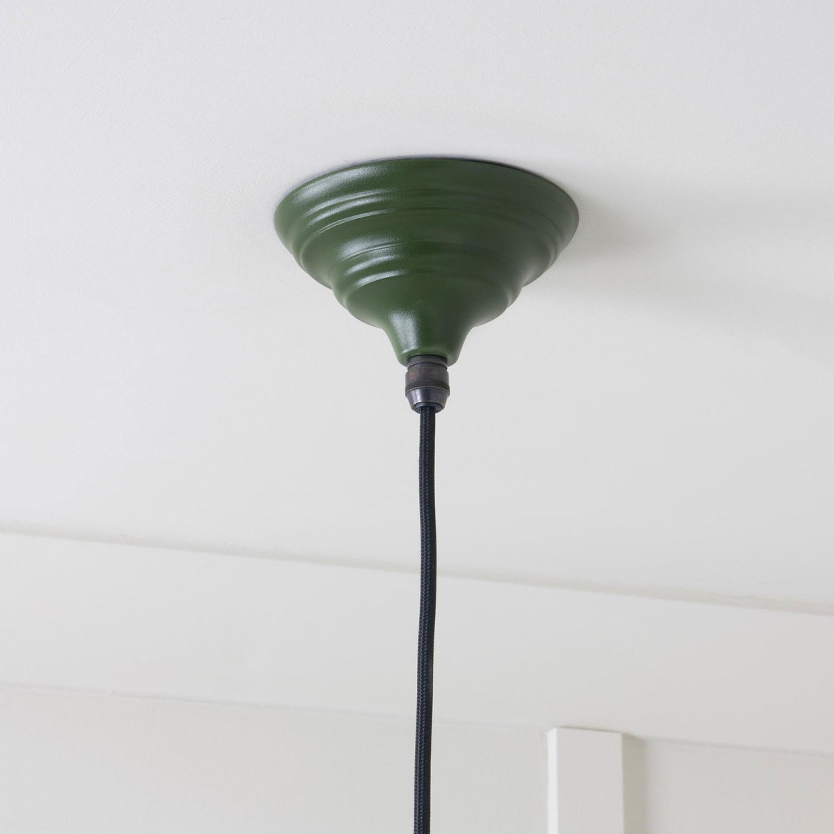 A dark green ceiling rose with a black braided cable extending from it.