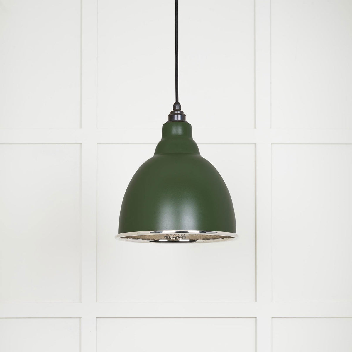 A dark green pendant light with a silver interior, shown against a panelled wall.