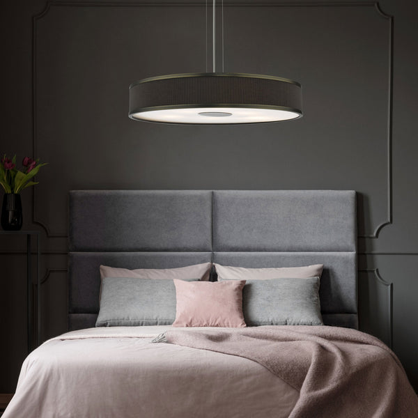 A modern bedroom with a dark gray wall, a gray upholstered headboard, and a bed with pink and gray bedding.