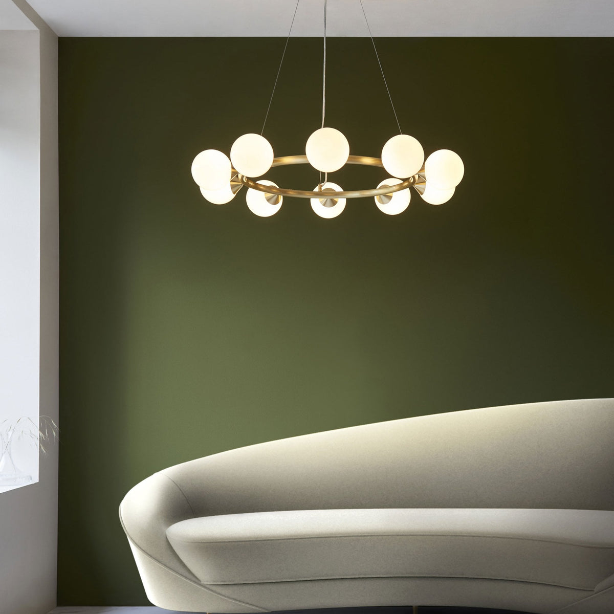 A modern brass chandelier with ten globe lights hangs above a stylish white sofa against a green wall.