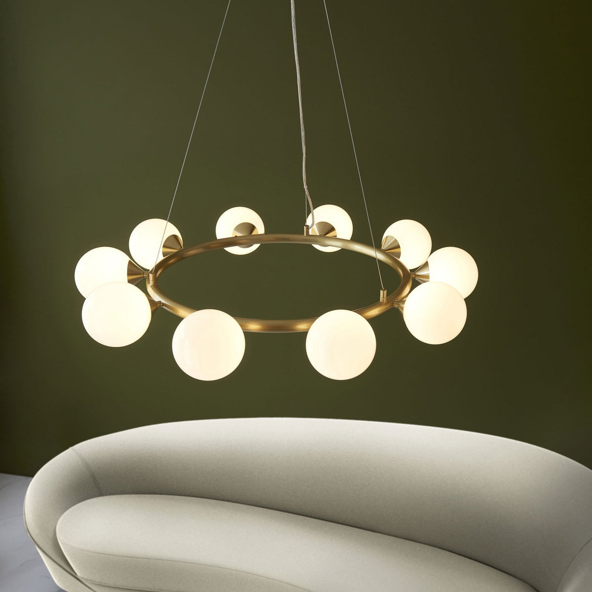 A brass chandelier with multiple globe lights illuminates a room with a white sofa and a green wall.