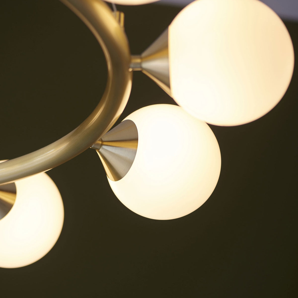 Detail of a brass chandelier arm with a glowing white globe light against a dark background.