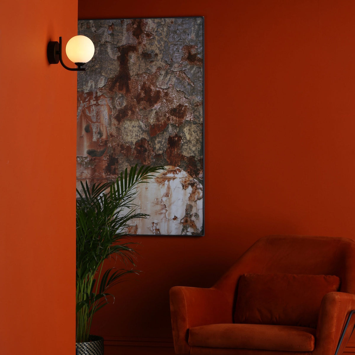 A modern living room with a burnt orange wall, a black wall sconce, and a rust-colored armchair.