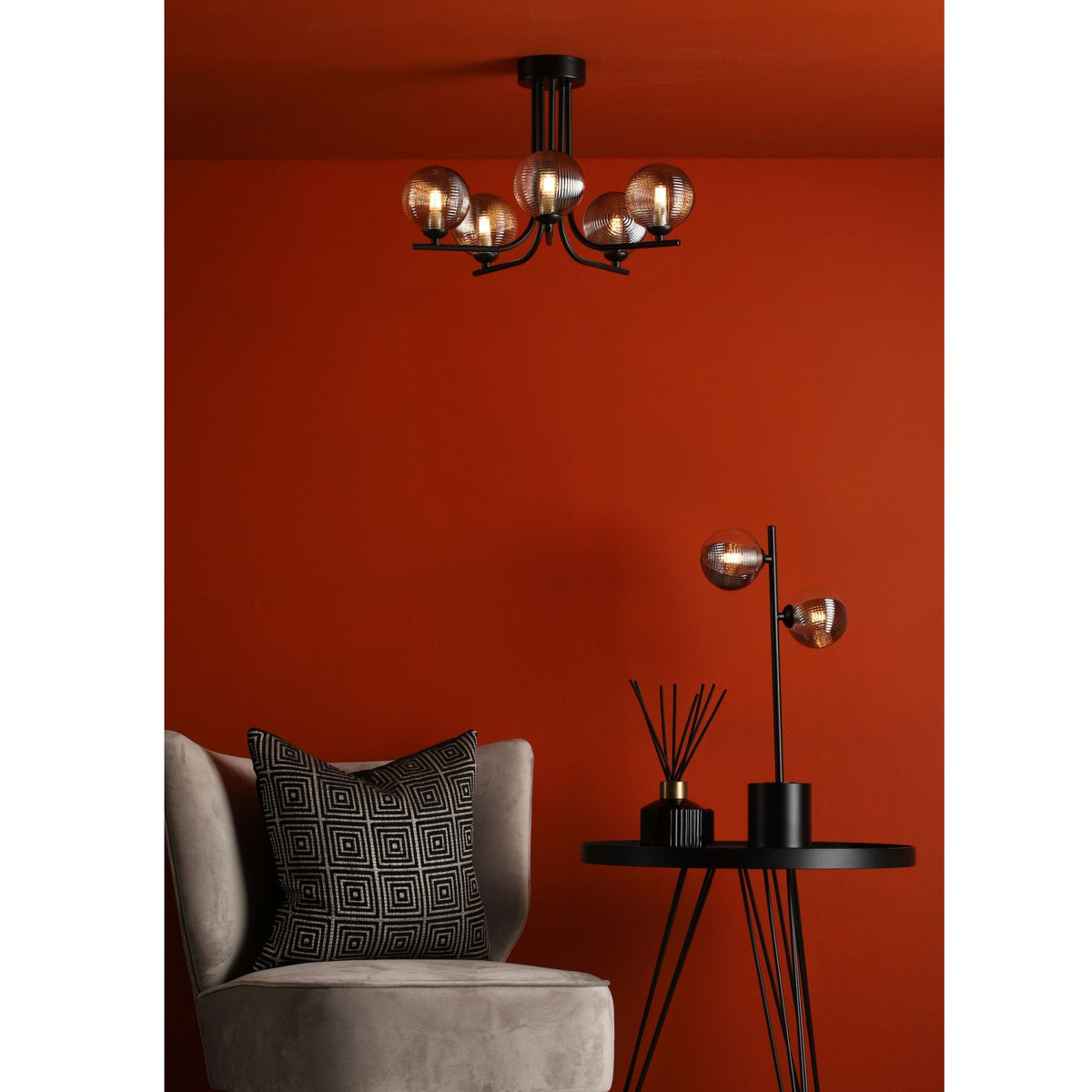 A modern living room with a red wall, a gray armchair, and a black side table with a lamp and diffuser.