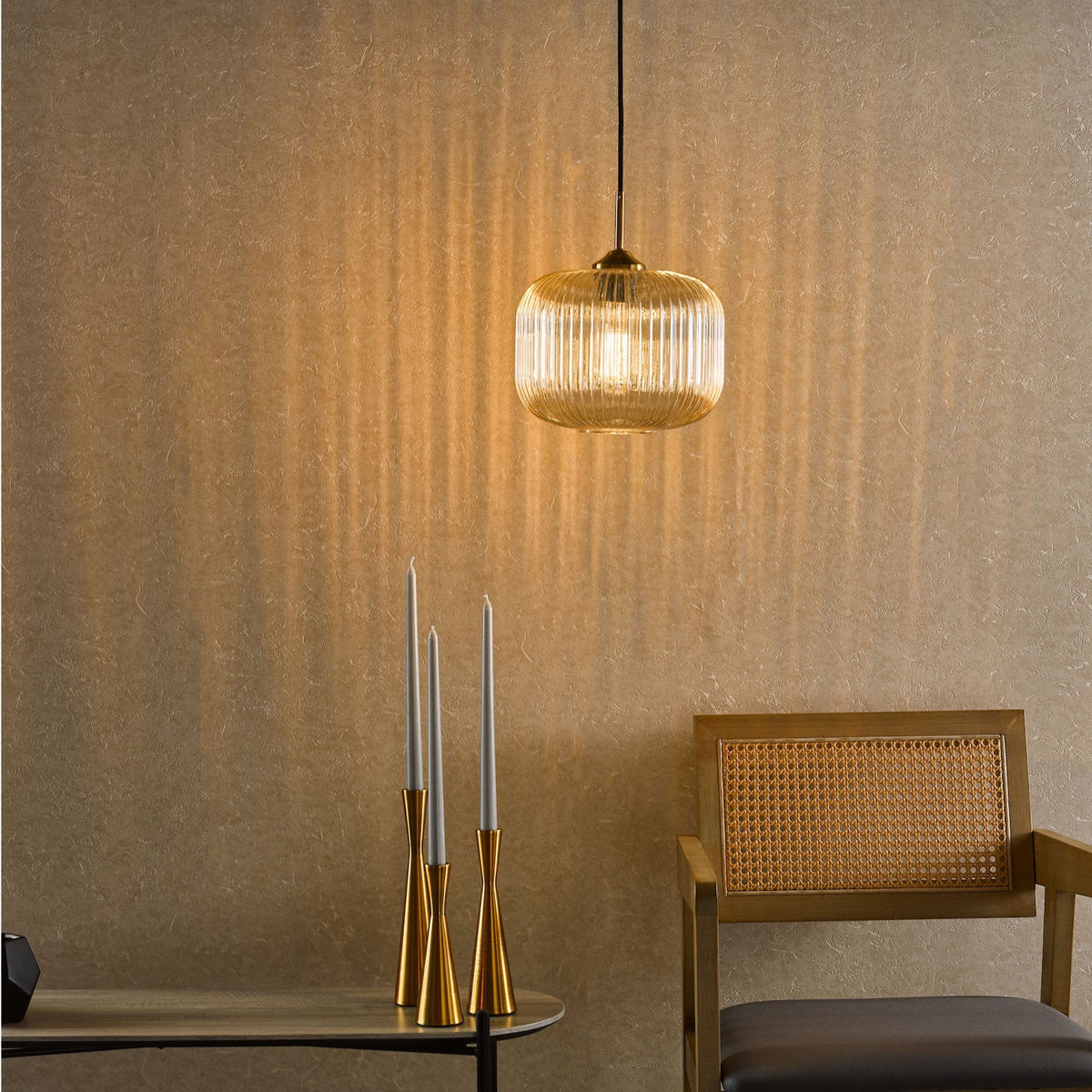 A ribbed glass pendant light hangs above a table with three gold candlesticks and a wooden chair.