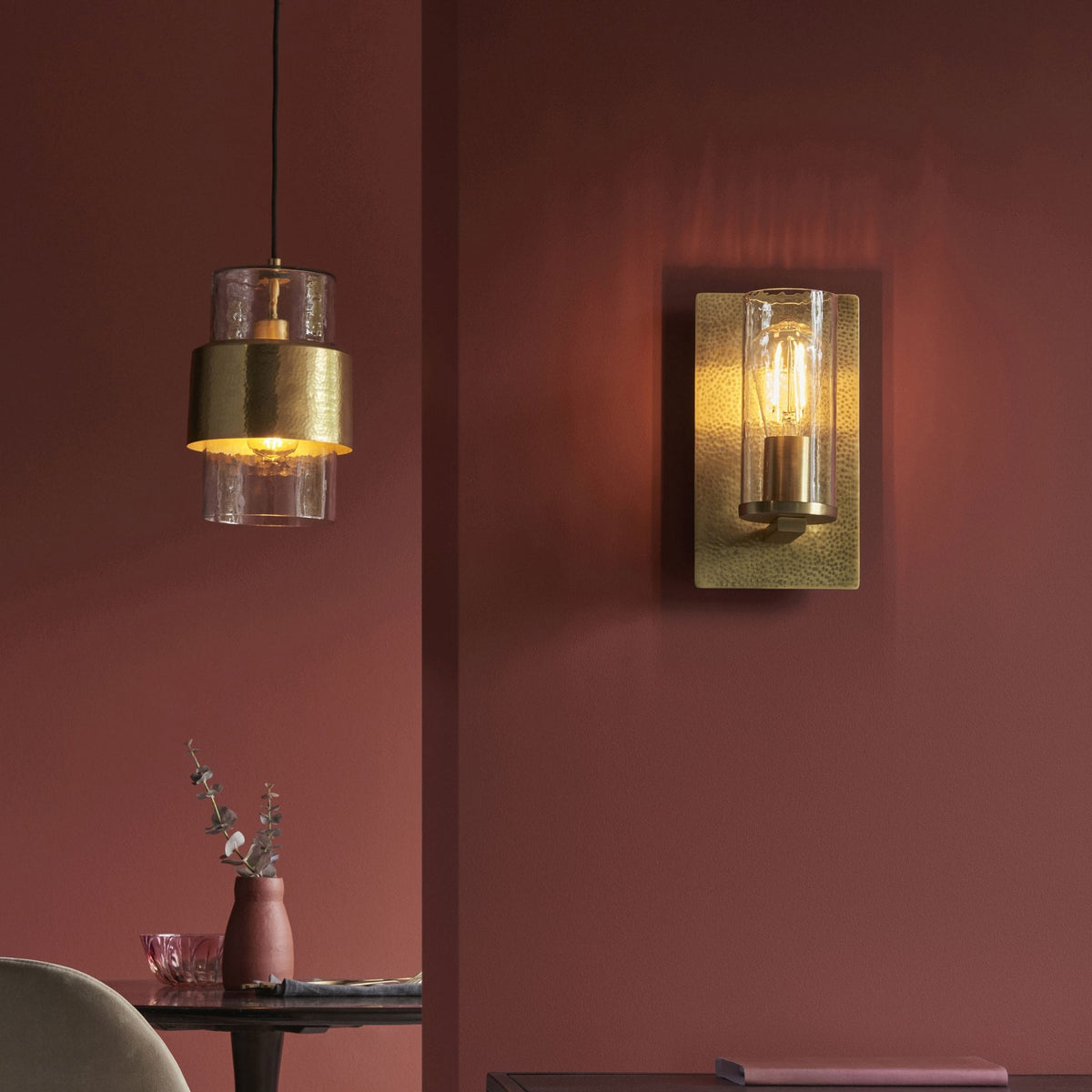 A wall sconce and a hanging pendant, both with glass and gold, provide warm light in a modern dining room.