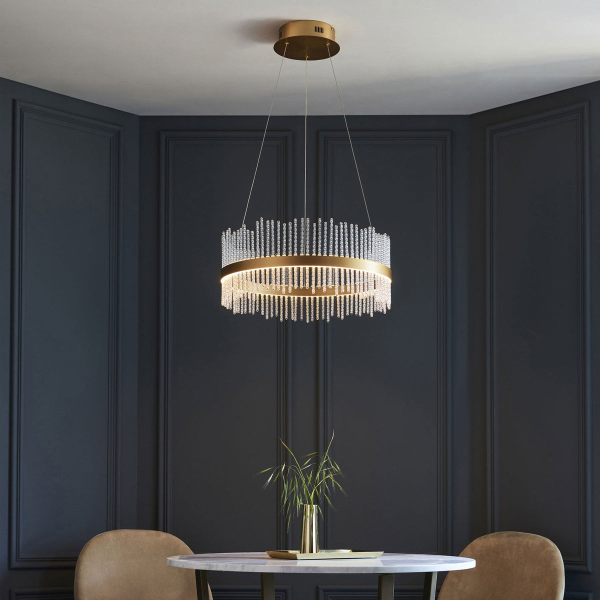 A brass chandelier with hanging glass rods illuminating a dining area with a round table and two chairs.