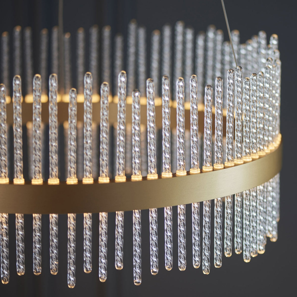 A close-up of a brass chandelier featuring clear, textured glass rods illuminated from within.