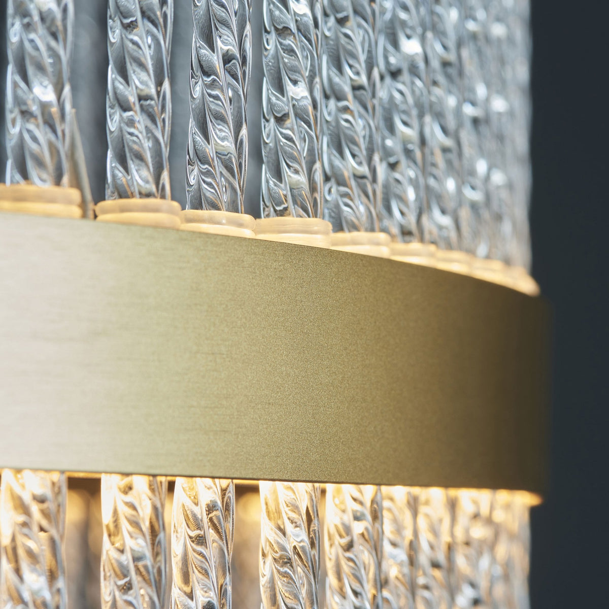 A close-up of the brass band and textured glass rods of a modern chandelier, showing intricate details.