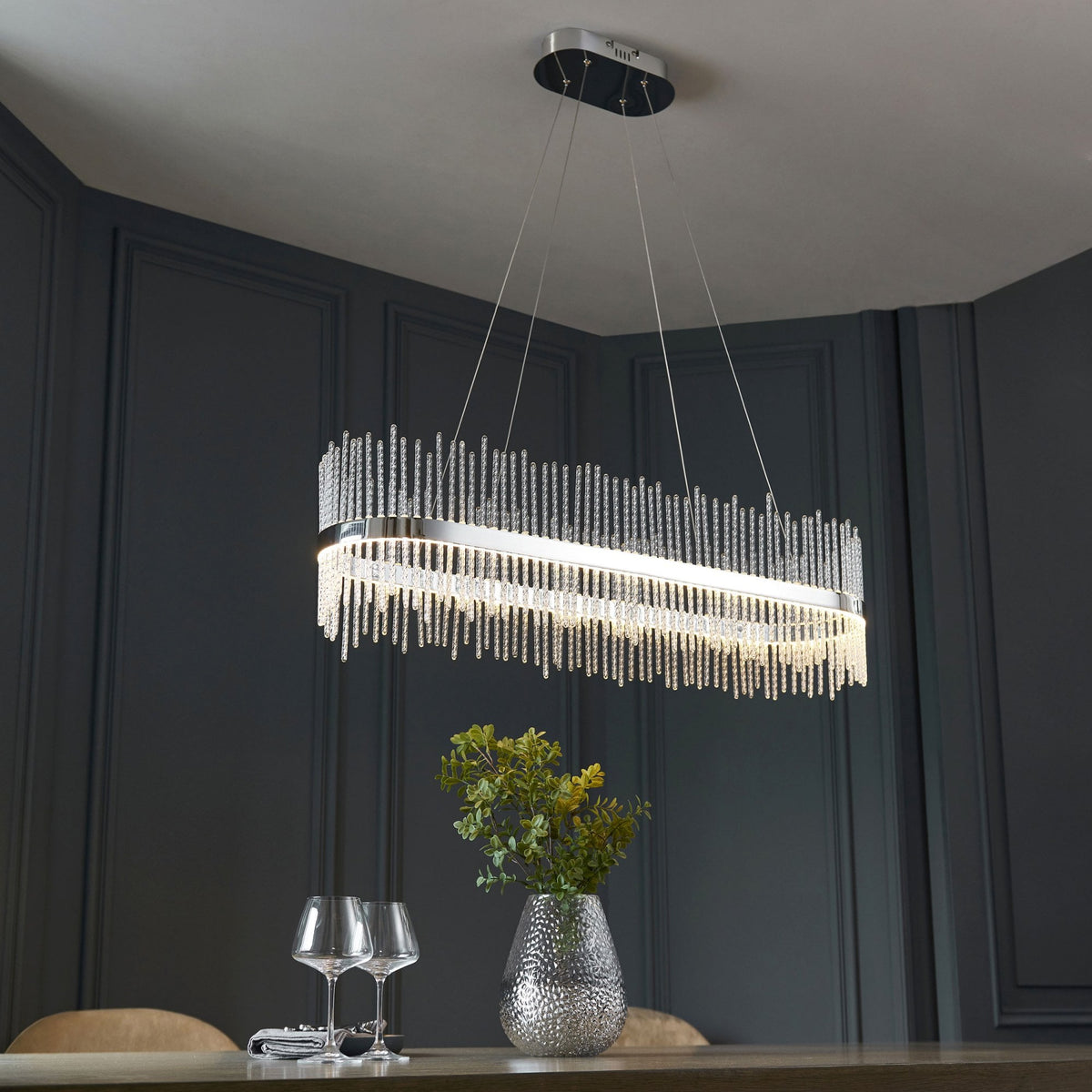 A modern dining room with a long, rectangular chandelier, showcasing its elegant design and soft illumination.