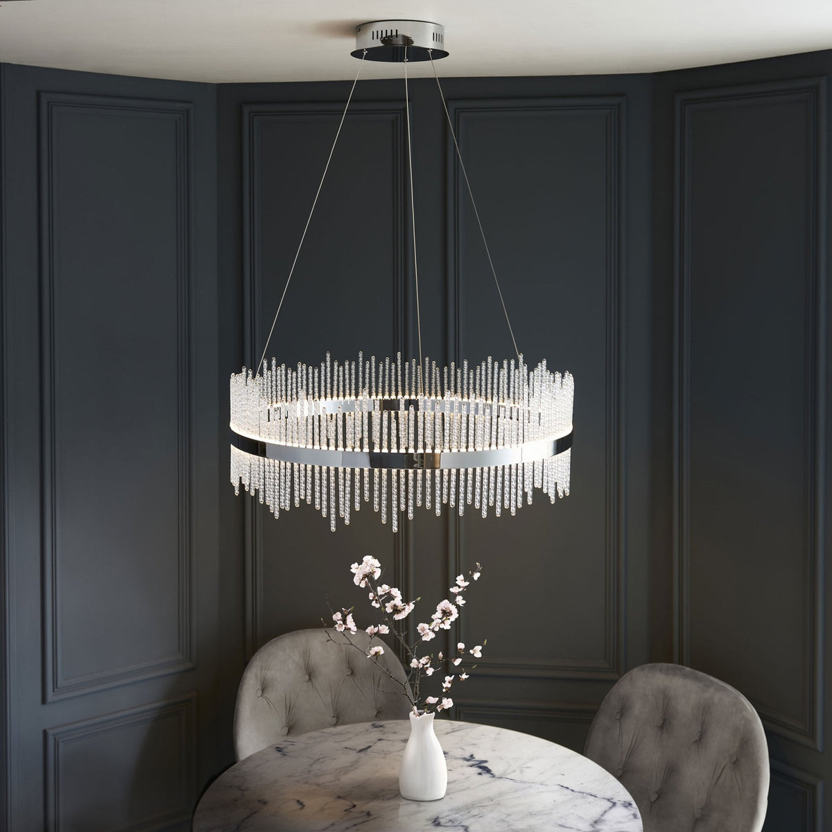A sophisticated crystal chandelier hangs over a modern dining table, casting a warm glow on the room.