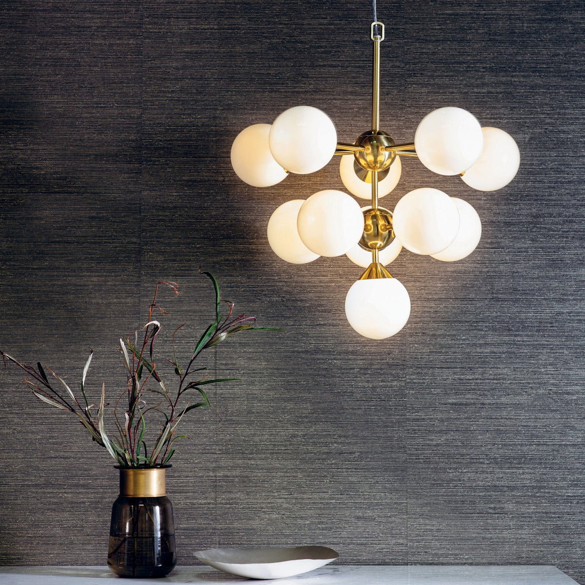 A brass chandelier with ten white globe lights hangs over a table with a vase of greenery.