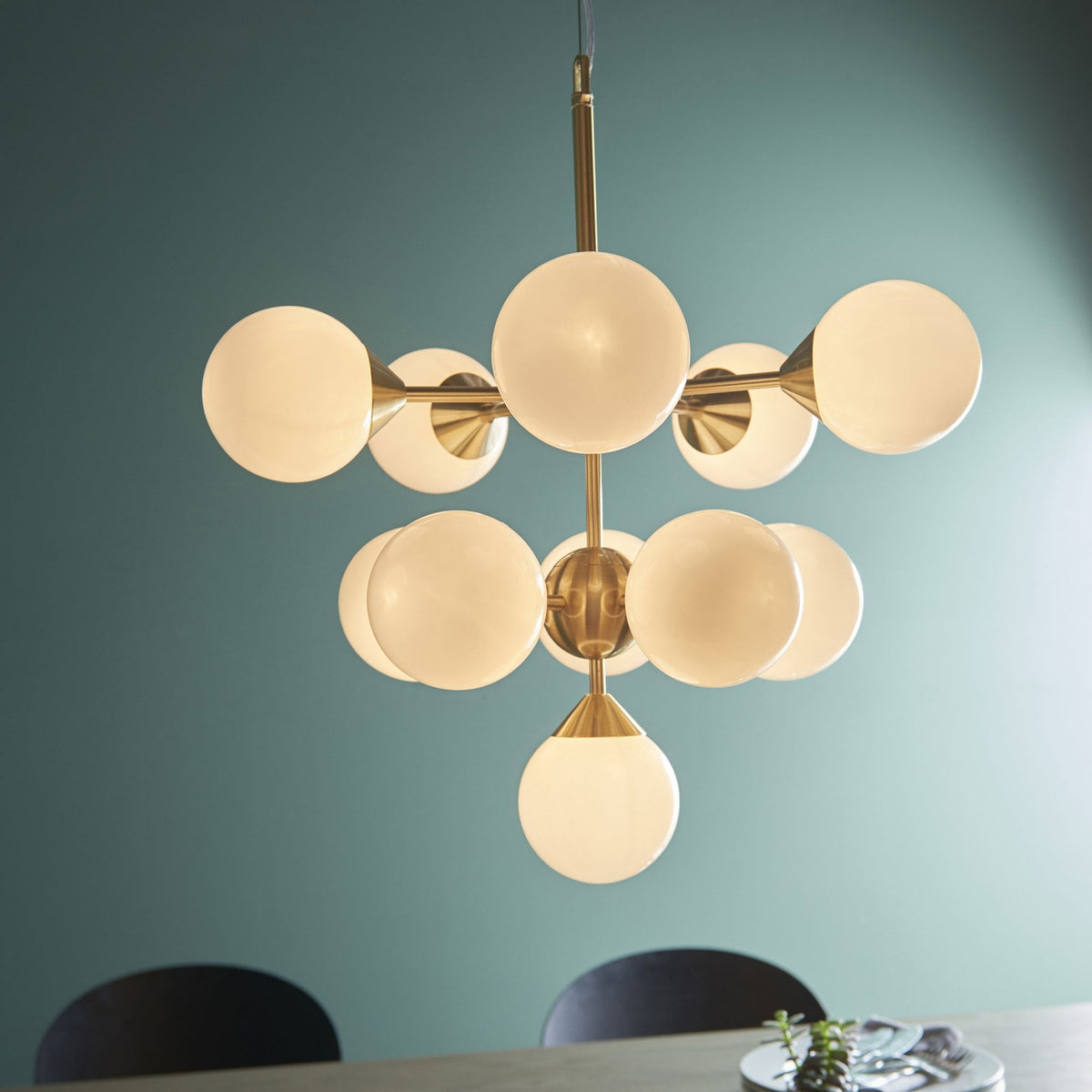 A brass chandelier with ten white globe lights illuminates a room with teal walls.